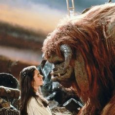 a woman standing next to a giant creature in front of a man with long hair