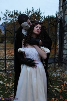 a man and woman dressed up as dracula and bride hugging in front of a gate