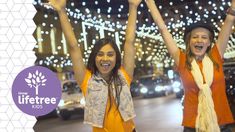 two women standing in the street with their arms up and hands raised above their heads