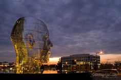 a large glass sculpture in front of a building at night with the sun setting behind it