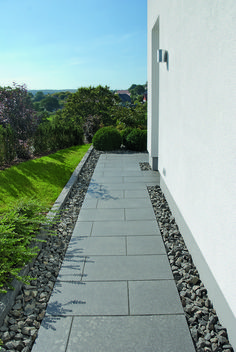 an empty walkway between two buildings with grass and bushes in the backrounds