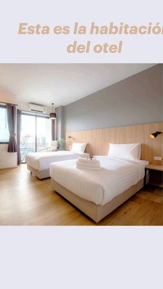 two beds in a hotel room with wooden floors and large windows overlooking the cityscape