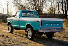 a blue and white ford truck parked on a dirt road