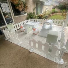 an outdoor play area with white fence and wooden toys on the ground in front of a house