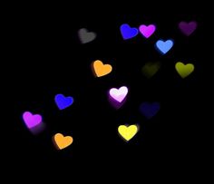 many different colored hearts floating in the air on a black background with some blurry lights