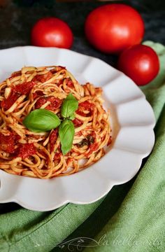 a plate of spaghetti with tomato sauce and basil leaves on top, next to tomatoes