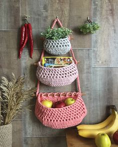 three crocheted baskets are hanging on the wall next to some fruit and vegetables