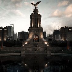 a statue with a bird on top in front of a cityscape at night