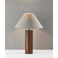 a wooden table lamp with a white shade on it's base and a grey wall in the background