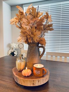 a wooden table topped with a vase filled with leaves and two lit candles on top of it