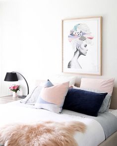 a bed with pillows and blankets on top of it next to a painting hanging above the headboard