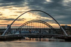 a large bridge spanning over a river with tall buildings in the background and clouds in the sky