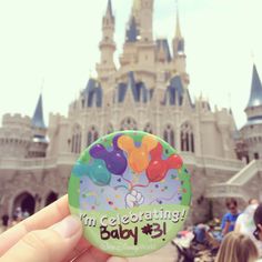 a person holding up a button with the words i'm celebrating baby in front of a castle