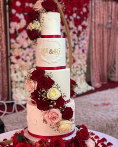 a three tiered wedding cake with red and white flowers on the table in front of a floral wall