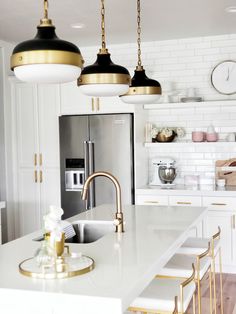 a white kitchen with gold accents and pendant lights hanging from the ceiling over the sink