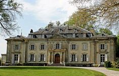 an old building with many windows in front of it on a green lawn surrounded by trees