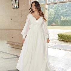 a woman in a long white dress is smiling and looking at the camera while standing outside