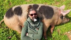 a woman wearing sunglasses standing next to a pig on top of a lush green field