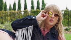 a woman with sunglasses and a flower on her eyeglasses is sitting in the grass