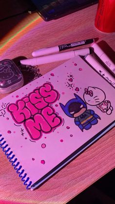 a pink notebook sitting on top of a wooden table next to a cell phone and pen