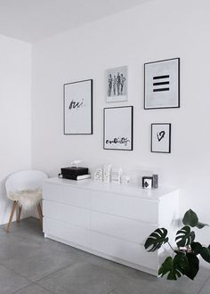 a living room with white furniture and pictures on the wall above it, along with a potted plant