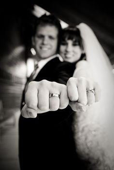 a bride and groom posing for a photo with their wedding rings on their fingers in black and white