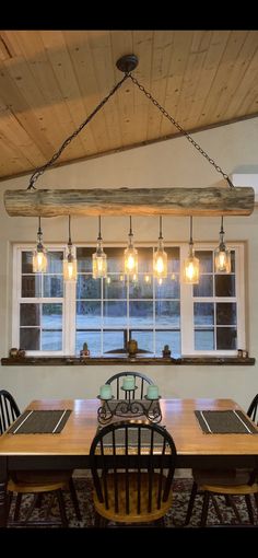 a dining room table and chairs with lights hanging from the ceiling above it in front of a window