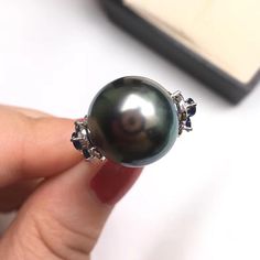 This is a stylish and beautiful ring earring. Product Information Origin Tahitian Pearl Jewelry Processed in Japan Material Tahitian Pearl and 18K White Gold Dimensions Custom Pearl Shaped: Round Size: 14-15mm Black Tahitian Pearl Quality: AAAA Nacre: Very Thick Color: Black with Peacock Green Luster Luster: Very High Accessories Metal: 18K White Gold Other: 0.60ct of SI Quality Natural Diamond and 1.80ct of Sapphire Luxury Tahitian Pearl Jewelry For Anniversary, Luxury Tahitian Pearl Anniversary Jewelry, Tahitian Pearl Gemstone Jewelry, Tahitian Pearl Jewelry With High Luster, Round Tahitian Pearl Gemstone Jewelry, Round Tahitian Pearl Jewelry With High Luster, Black Tahitian Pearl Ring, White Gold Tahitian Pearl Jewelry With High Luster, Tahitian Pearl Jewelry For Anniversary