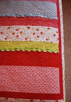 a close up of a quilted blanket on the floor with red, yellow and white stripes