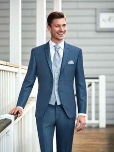 a man in a blue suit and tie standing on a porch with his hands in his pockets