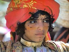 a woman wearing a red turban with gold decorations on her face and nose