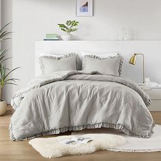 a bedroom with white walls and wooden flooring has a gray comforter on the bed