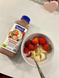 a bowl of strawberries and bananas next to a bottle of naked peanut butter on a table