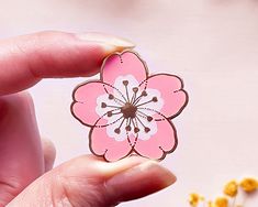 a hand holding a pink flower shaped sticker next to some yellow and white flowers