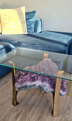 a glass table with a purple rock on it in front of a couch and pillows