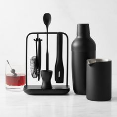 black kitchen utensils and bottles on a white countertop with a drink in the foreground