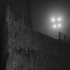 two headlights are shining in the fog over a wall and railing on a dark, foggy night