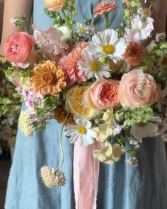 a woman in a blue dress holding a bouquet of pink and white flowers with an orange ribbon