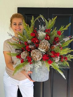 a woman standing in front of a door holding a bucket filled with red and white flowers