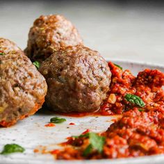 three meatballs on a plate covered in sauce