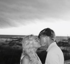 a man and woman kissing in front of a cloudy sky