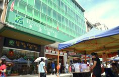 people are walking in front of the hotel central on a busy street with umbrellas