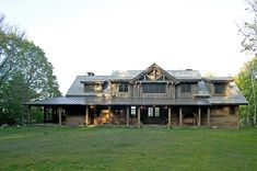 a large wooden house sitting in the middle of a lush green field with lots of trees