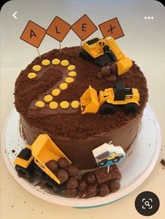 a chocolate cake decorated with construction vehicles and nameplates on the top, sitting on a plate