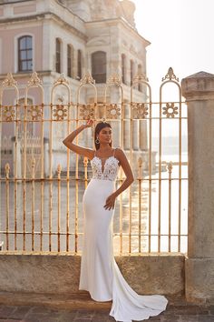 a woman in a white wedding dress standing by a fence with her hand on her head