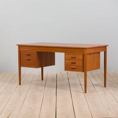 a wooden desk sitting on top of a hard wood floor next to a white wall