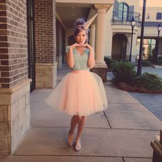 a woman standing on the sidewalk wearing a pink tulle skirt and crop top with her hands to her face