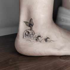 a small black and white tattoo on the foot of a person with a dolphin in the water