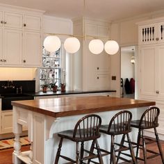 a kitchen island with three stools in front of it and lights hanging from the ceiling