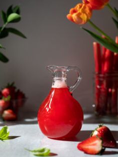 a red vase filled with liquid next to some strawberries